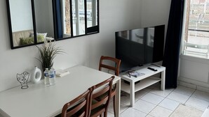 Un soggiorno moderno con zona pranzo, un'ampia televisione a schermo piatto e vista sulla città dalla finestra.