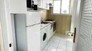 Una cucina compatta con mobili bianchi, lavatrice, fornello e lavandino.