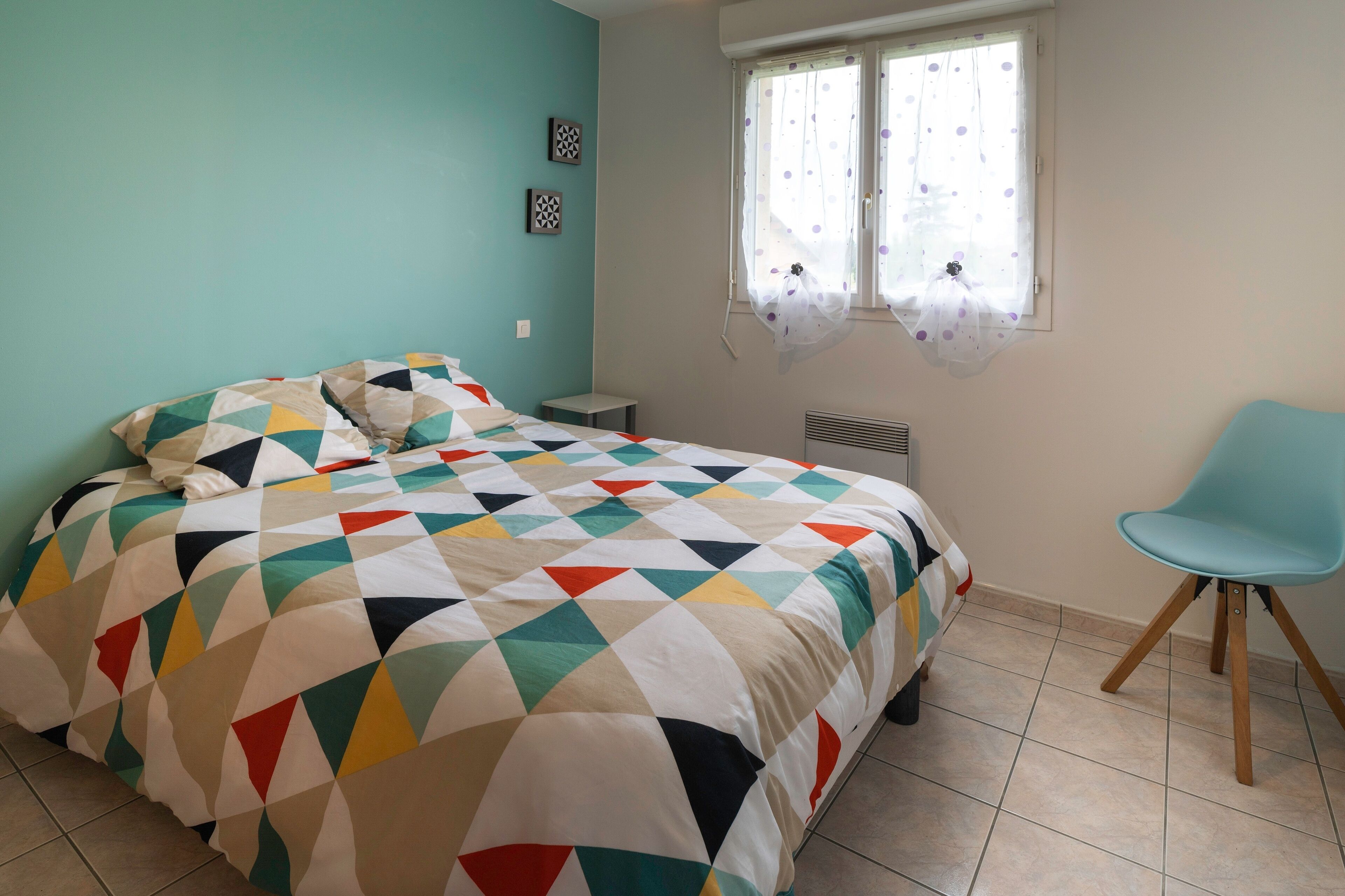 A bedroom with a bed, a chair, a window with curtains, and a radiator.