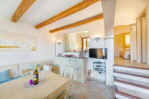 A cozy living room with a dining area, wooden beams, a TV, and a staircase leading to another room.