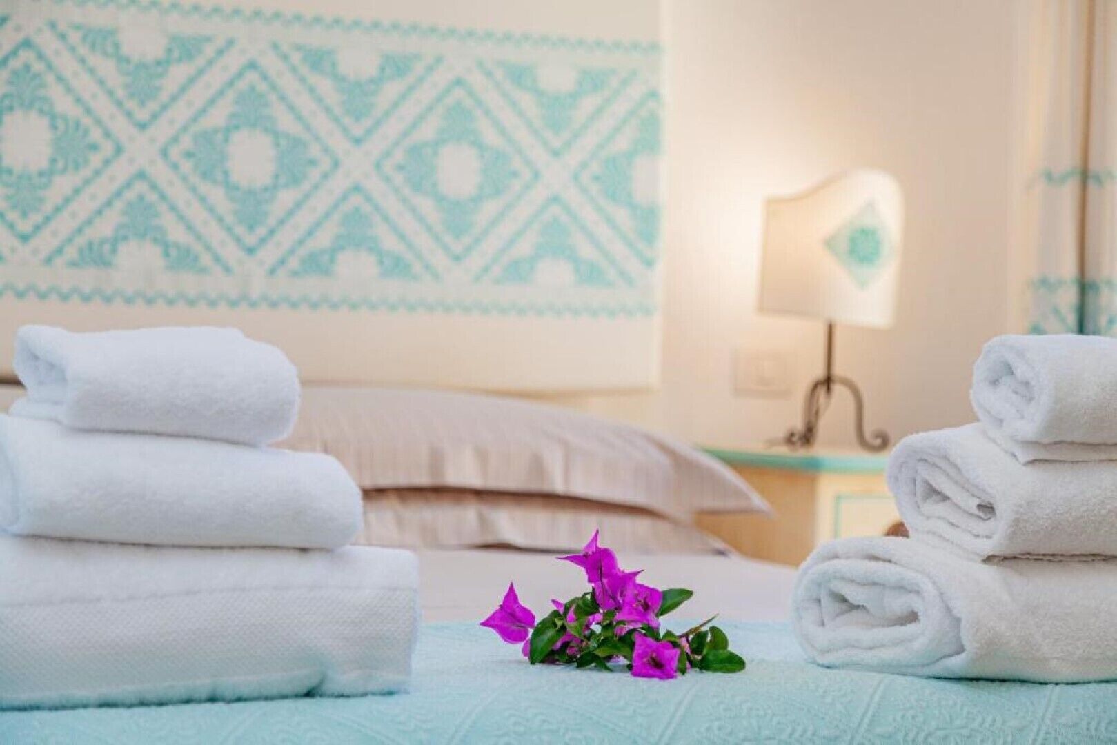 Un lit bien fait, avec du linge de lit blanc, un motif décoratif sur le mur et une lampe de chevet.