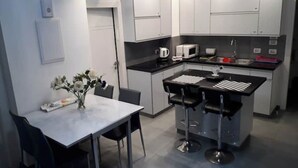 Une cuisine moderne avec des meubles blancs, un plan de travail noir, une machine à café, un four à micro-ondes et un évier. On y trouve une table à manger avec deux chaises et un vase rempli de fleurs.