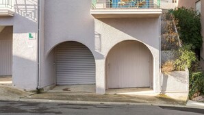 A multi-story building with a light-colored facade, green balconies, and a garage door. - Le Petit Colliourenc - Apt climatisé avec terrasse (Collioure)