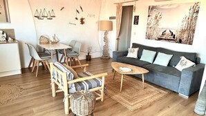 A modern living room with a grey sofa, wooden floor, and a dining area with a table and chairs. - Le Petit Colliourenc - Apt climatisé avec terrasse (Collioure)