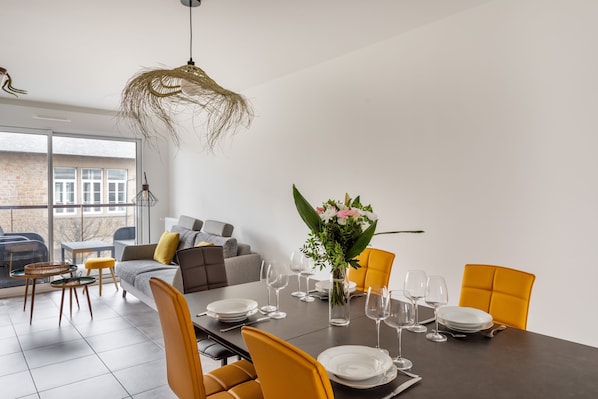 A modern dining area with a dark table set for six, surrounded by yellow chairs.