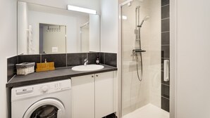 A modern bathroom with a washing machine, a sink, and a glass-enclosed shower.