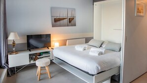 A modern bedroom with a bed, bedside table, TV, and a painting on the wall. - Quo Vadis - Proche plage et parking privé (Arcachon)