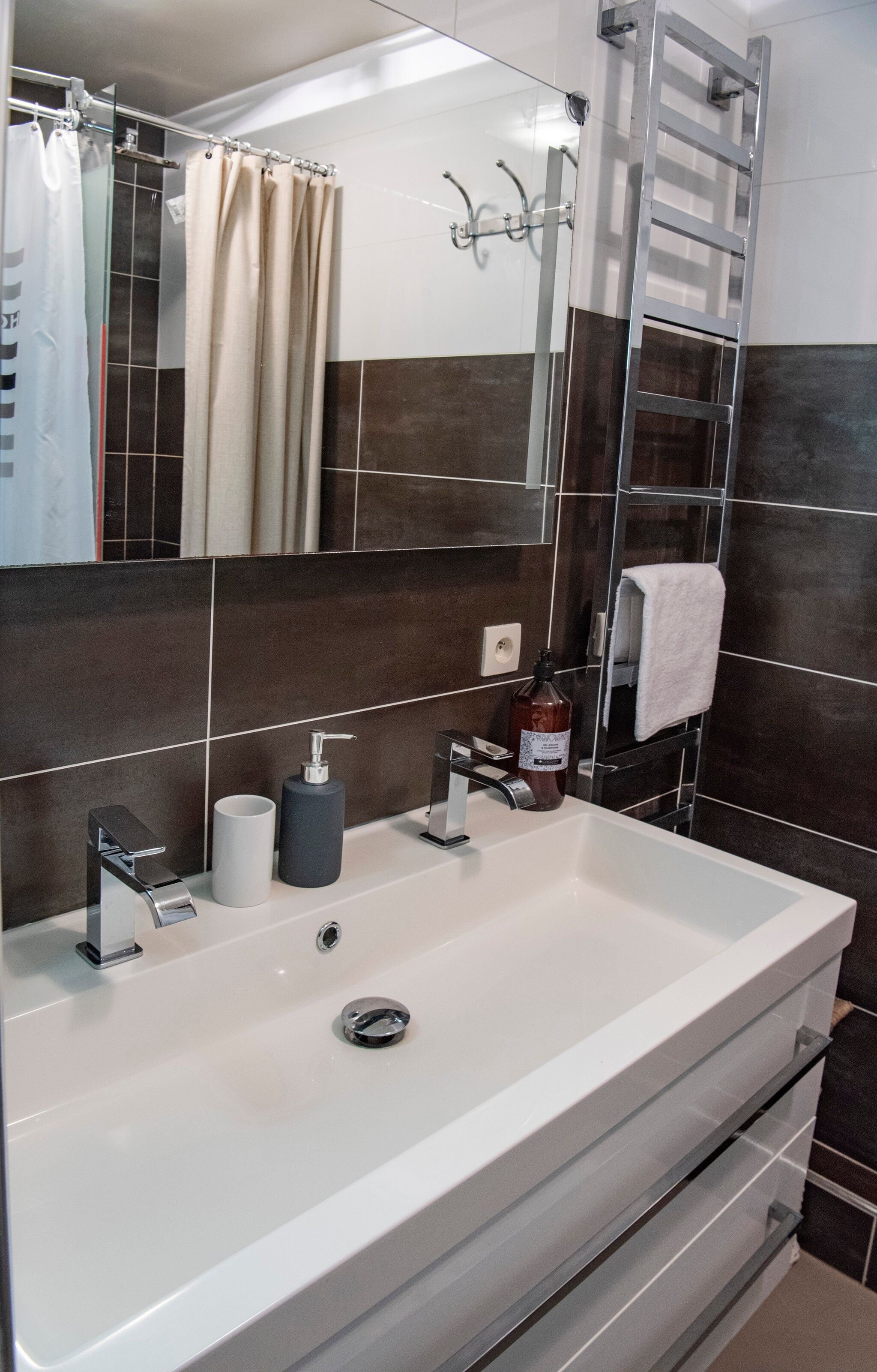 Ein modernes Badezimmer mit einem großen, weißen Waschbecken, einem Spiegel, einer Duschvorhang, einem Handtuchhalter und einer Handseifenflasche.