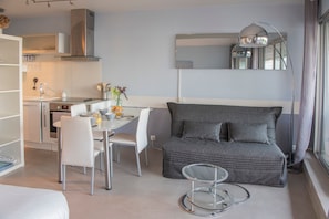 A modern hotel room with a kitchenette, a dining area, a grey sofa, and a glass coffee table.