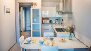 A modern kitchen with white cabinets, a dining table set for two, and a vase with flowers on the counter. - Quo Vadis - Proche plage et parking privé (Arcachon)