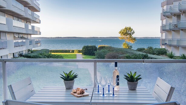 A balcony with a table set for two, potted plants, and a bottle. - Quo Vadis - Proche plage et parking privé (Arcachon)