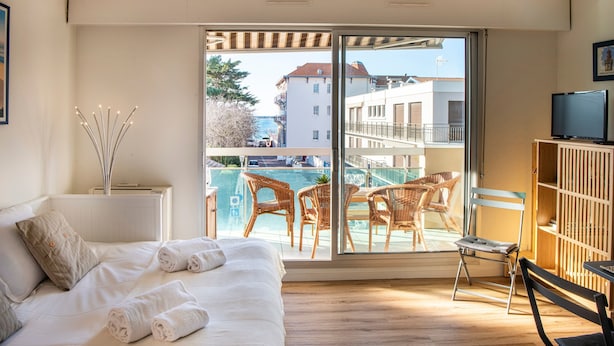 Un dormitorio con cama, televisor y balcón con mobiliario de mimbre y vista a la piscina.