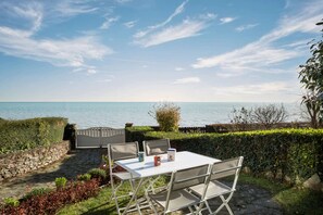 Ein Sitzbereich im Freien mit Tisch und Stühlen, einem Steinweg und Blick auf das Meer.