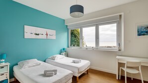 Une chambre avec deux lits, un bureau et une fenêtre donnant sur la mer.