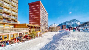 Et hotel med flere etager, udendørs siddepladser og en ski-bakke i baggrunden.
