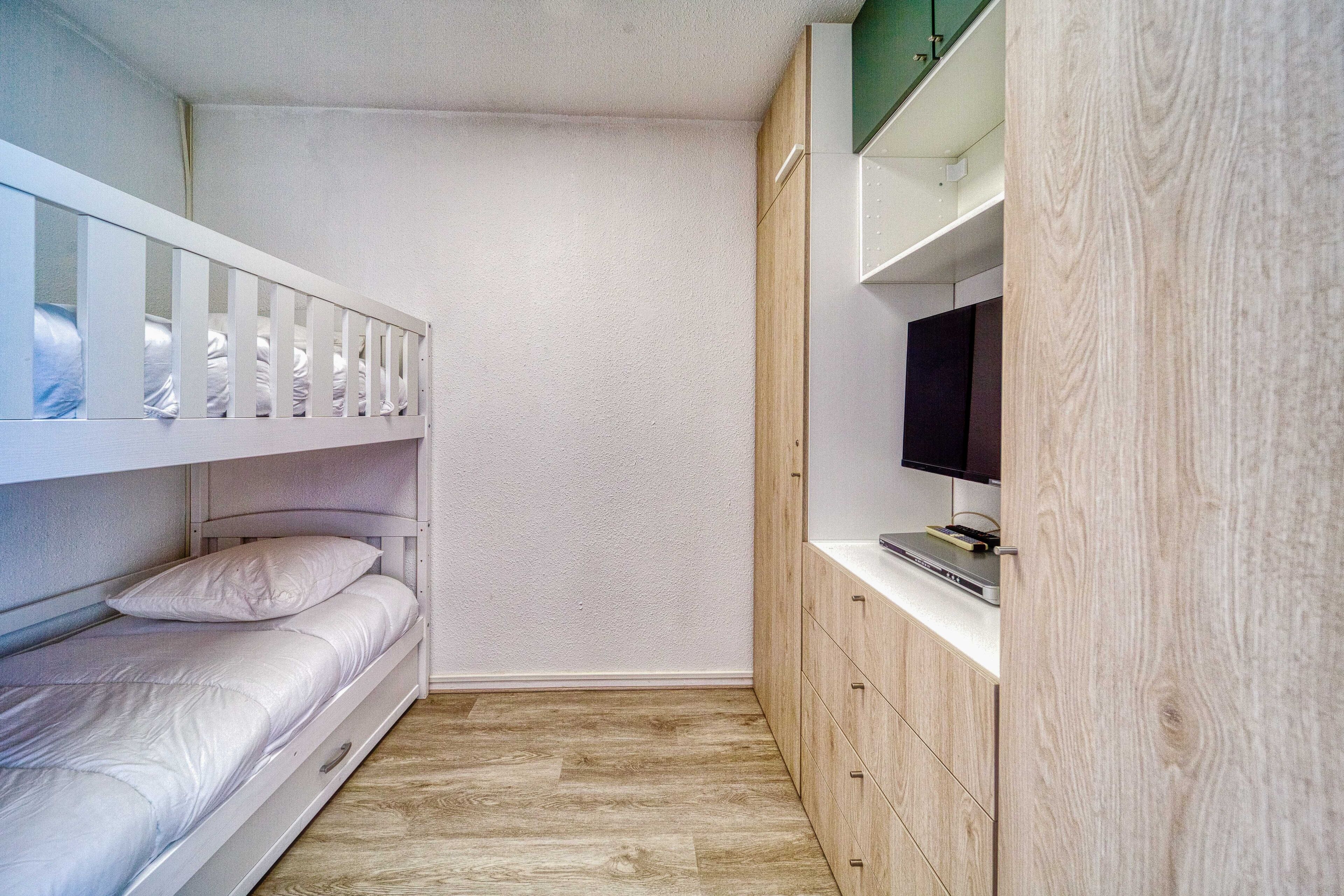 Une chambre avec des lits superposés, une télévision et des armoires en bois.