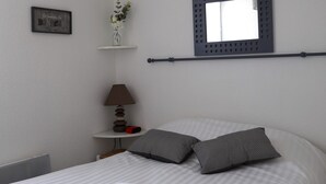 Ein ordentlich gemachtes Bett mit aufgerollten Handtüchern, einer Nachttischlampe, einer kleinen Ablagefläche mit einer Pflanze und einem an der Wand befestigten Spiegel.