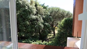 Blick aus einem Fenster mit einem Holzbalkon auf einen Garten mit verschiedenen Bäumen und Sträuchern.