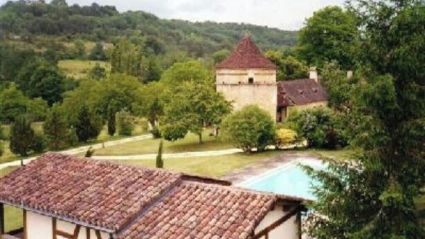 A traditional building with a red-tiled roof, surrounded by lush greenery and a swimming pool. - Le Pigeonnier (Plazac)