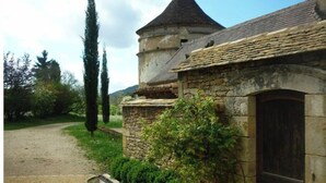 A stone building with a tower, a gravel path, and greenery. - Le Pigeonnier (Plazac)