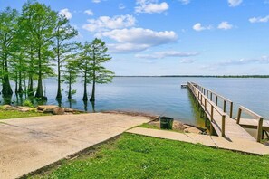 A concrete dock extending into calm water with trees on the opposite shore. - Lakefront Hotel Room w/ Private Pier & Boat Ramp (Vicksburg)