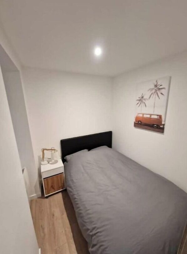 A small, neatly arranged bedroom with a single bed, a nightstand, and a wall-mounted picture of a car and palm trees.