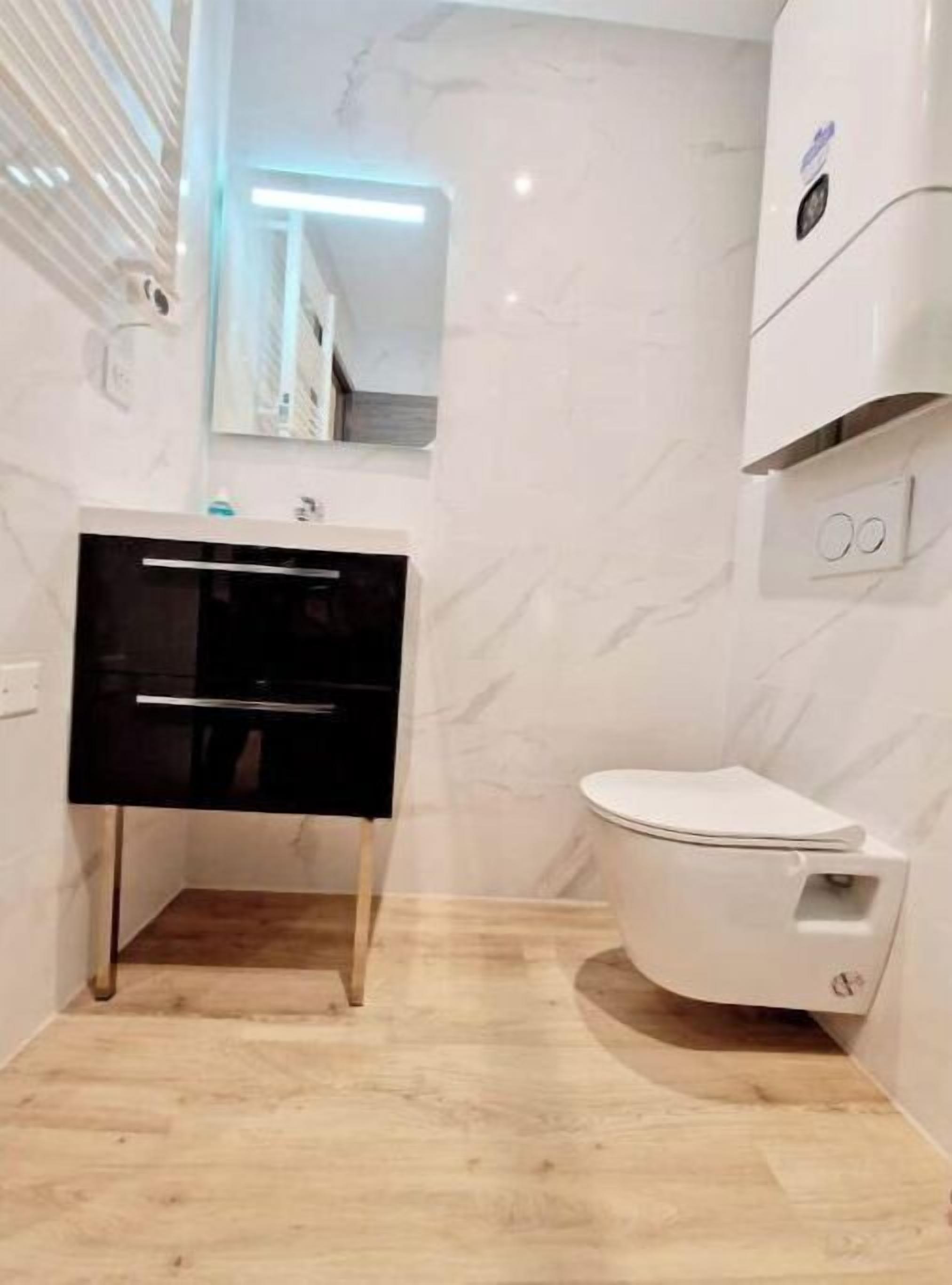 Un baño moderno con inodoro blanco, tocador negro y espejo sobre el lavamanos.