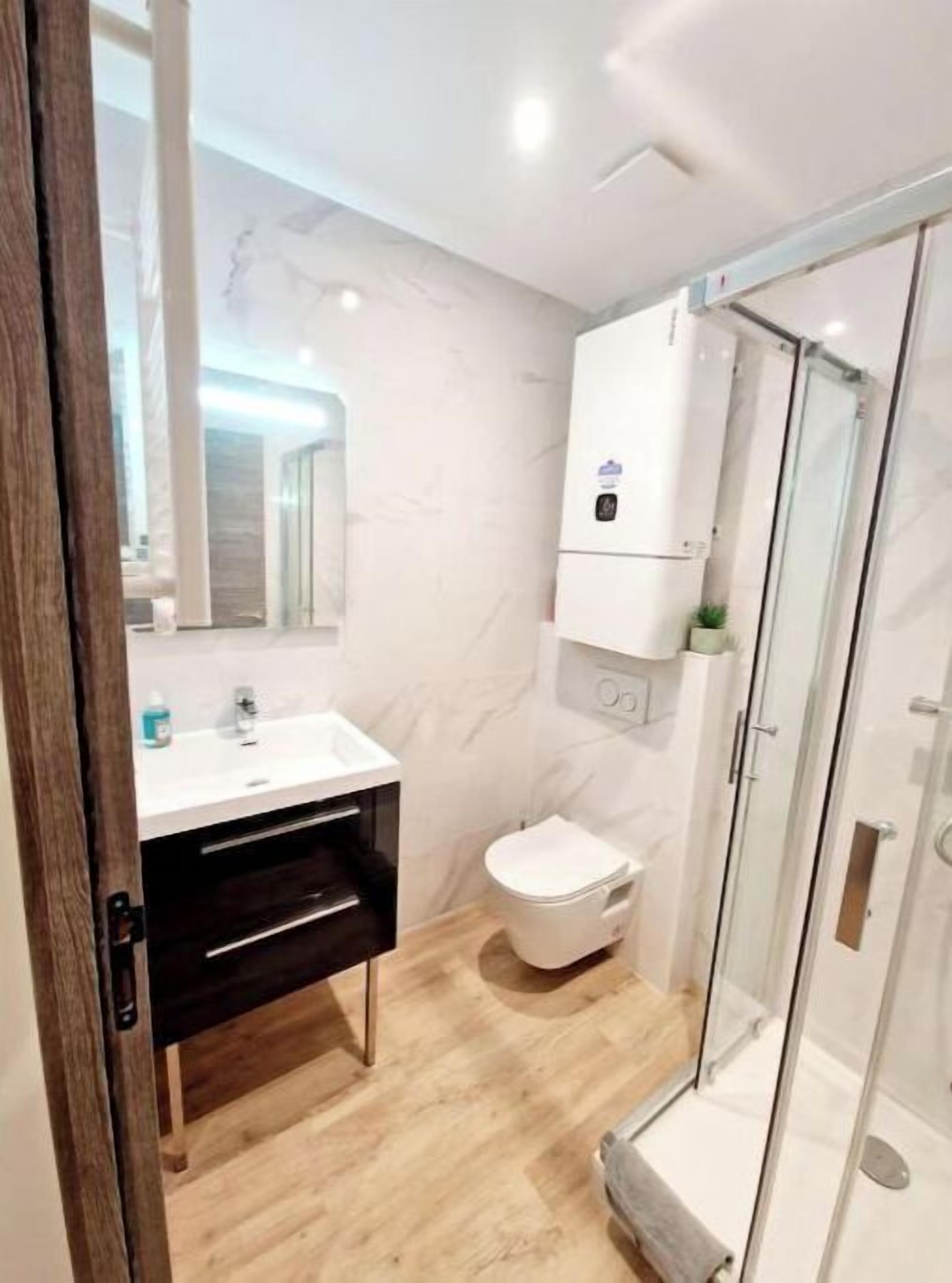 Ein modernes Badezimmer mit Waschbecken in Weiß, dunklem Holzschrank, Toilette in Weiß und einer Duschkabine aus Glas.