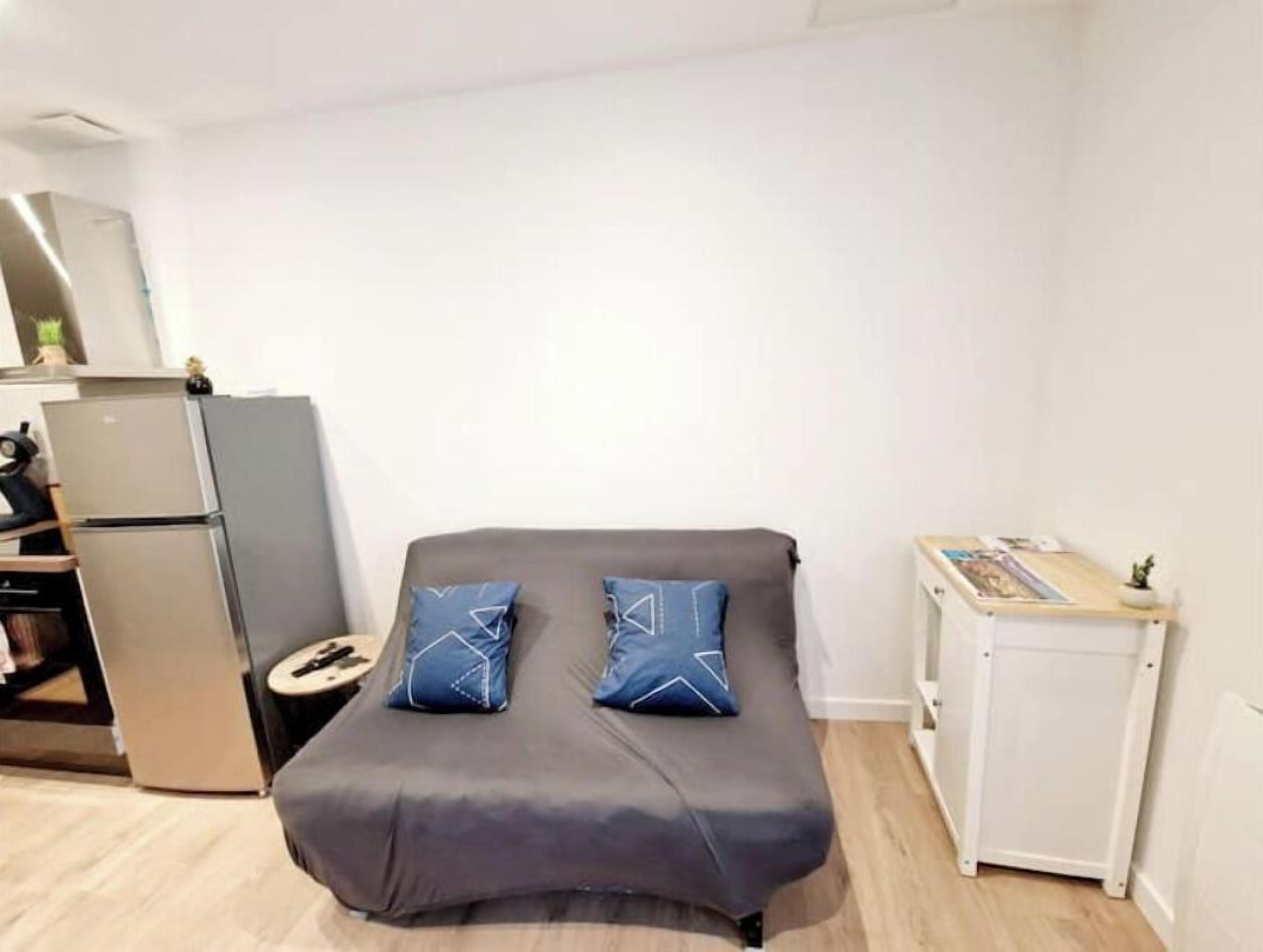 A compact bedroom with a bed, a small bedside table, a refrigerator, and a cabinet.