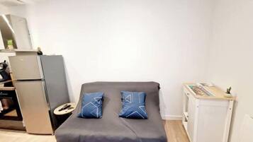 A compact bedroom with a bed, a small bedside table, a refrigerator, and a cabinet.