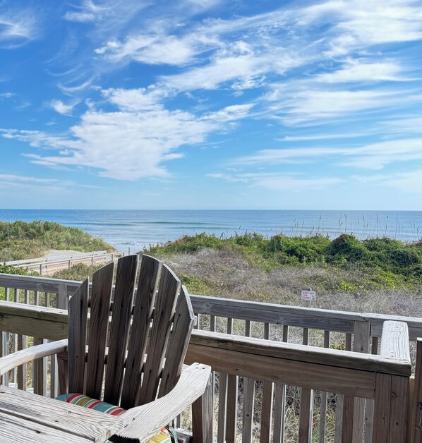 A wooden deck with a chair facing a beach view.