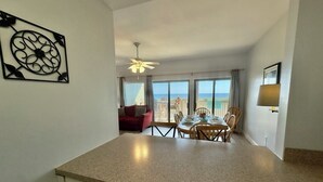 A spacious room with a kitchen area, dining table, and a view of the ocean.