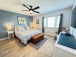 A bedroom with a bed, bedside tables, a ceiling fan, a window with blinds, and a TV on a stand.
