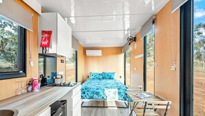 A compact room with a bed, a small kitchenette, and a window with a view of the outdoors. - Cabernet Tiny House by Tiny Away (Windeyer)