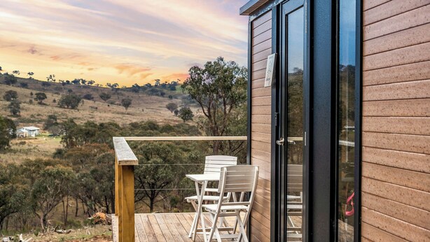 A wooden deck with a table and chairs, overlooking a hilly landscape. - Cabernet Tiny House by Tiny Away (Windeyer)