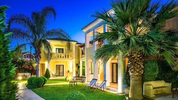Une maison à deux étages avec un jardin bien entretenu, un espace salon extérieur et un palmier.