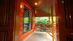A corridor with wooden flooring, a bench, and a view of greenery outside. - Entire Villa at the Heart of the Wayanad Forest. (Thirunelly)