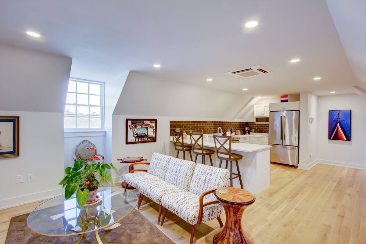 A modern kitchen with a refrigerator, a dining area with a sofa and chairs, and a large window providing natural light.