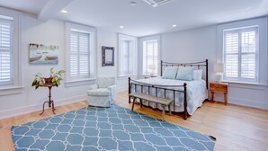 A bedroom with a large bed, a chair, a bedside table, and a window with shutters. - The Charleston Chestnut Mansion (Charleston)