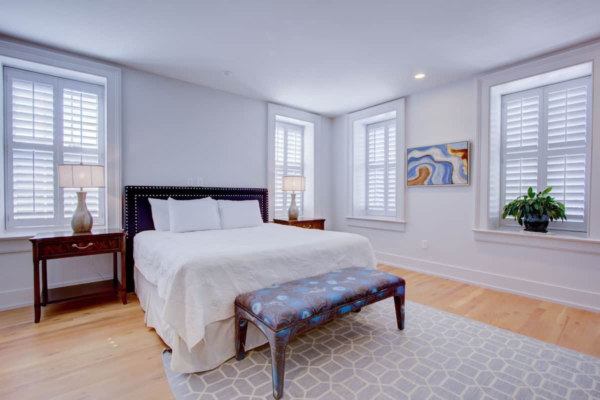 A bedroom with a bed, nightstands, a bench, and a window with blinds.