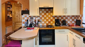 Una cocina compacta con armarios blancos, horno empotrado, cafetera y licuadora sobre la encimera.