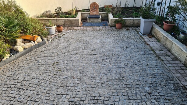Un patio empedrado con baldosas de piedra, plantas en macetas y una estructura de ladrillo.