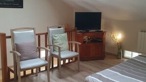 Un dormitorio con techo inclinado, dos sillones, una cama, un televisor y un armario pequeño.