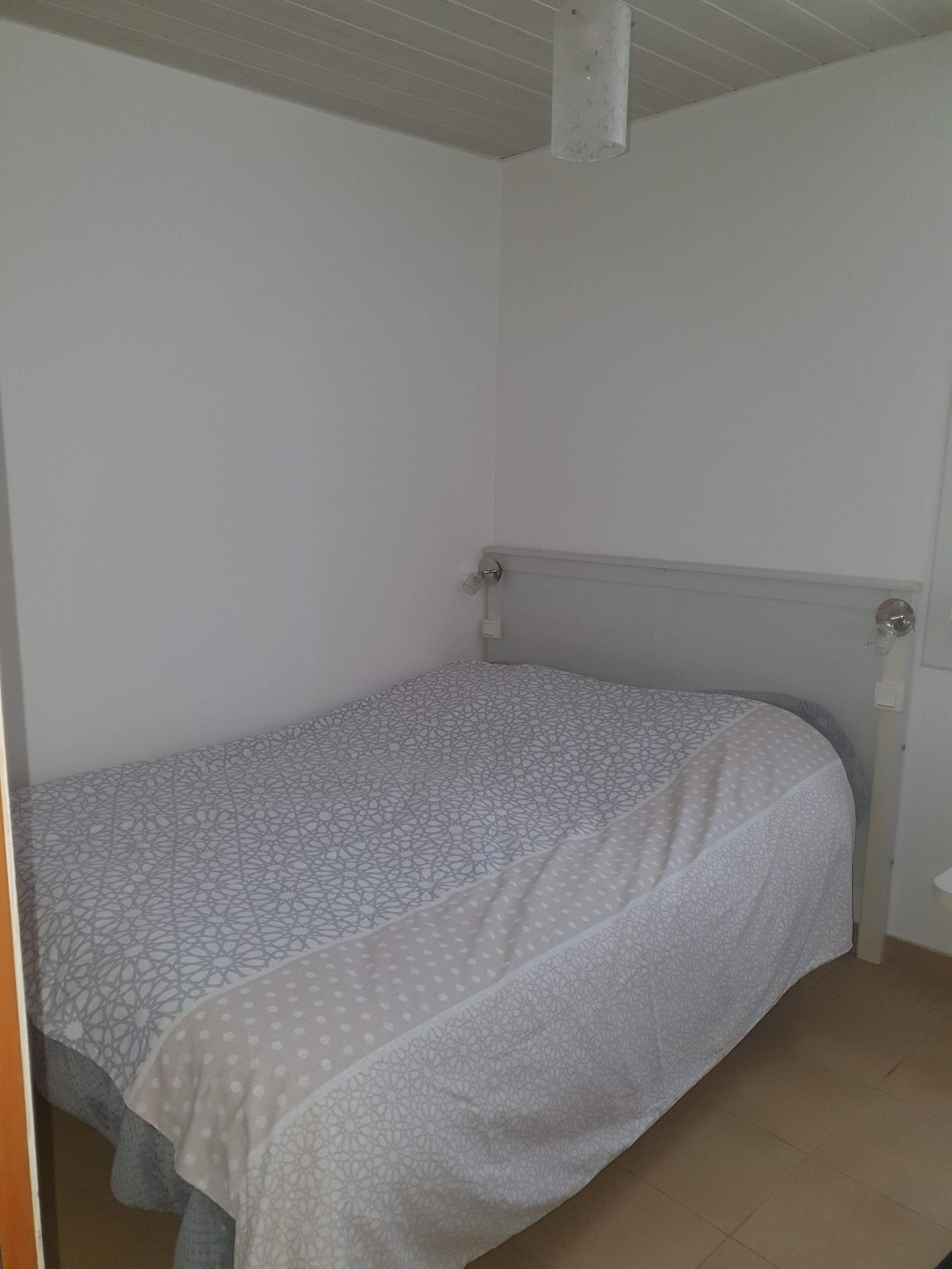 A small, single-bed room with a plain white wall and a simple, functional design.