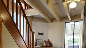 Una escalera que sube a un segundo piso, una chimenea, un comedor con una silla y un ventilador de techo.