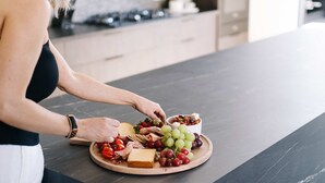 Iemand schikt een charcuteriebord in met kaas, druiven en andere ingrediënten op een houten plank.