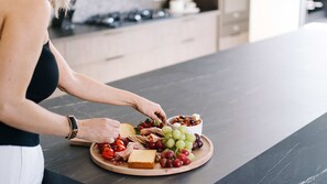 A person arranging a charcuterie board with cheese, grapes, tomatoes, and nuts on a wooden board.