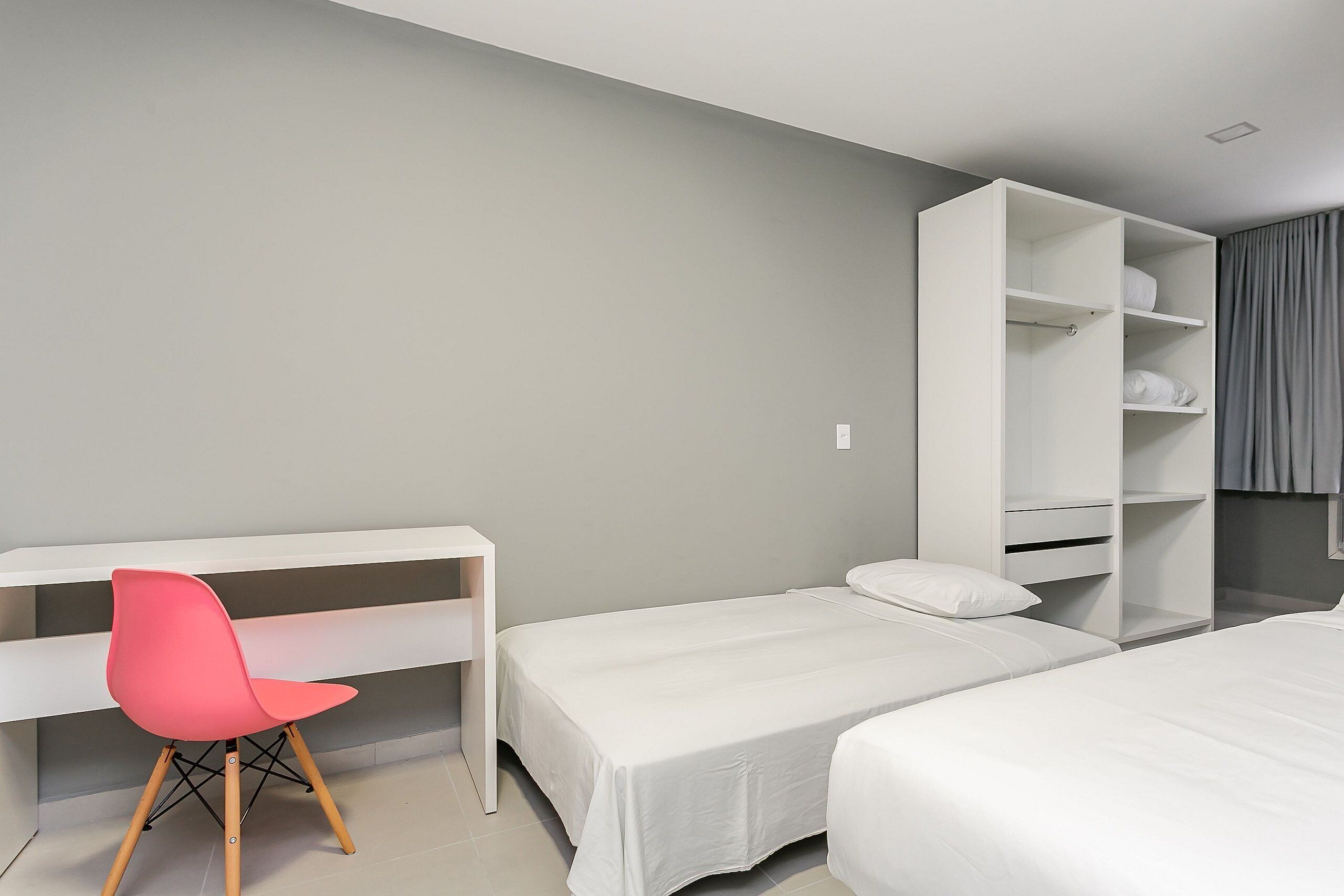 A room with two single beds, a white desk, a pink chair, and a white wardrobe.