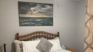 A bedroom with a wooden bed, a nightstand, a wall-mounted painting, and a ceiling fan. - Sizzling Hot Summer so stay by the Beach (New Smyrna Beach)