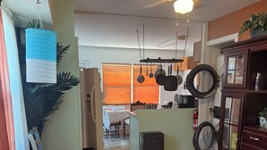 A cozy living room with a sofa, a small table, and a decorative plant. There is a kitchen area with a refrigerator, a sink, and a window with blinds. - Sizzling Hot Summer so stay by the Beach (New Smyrna Beach)